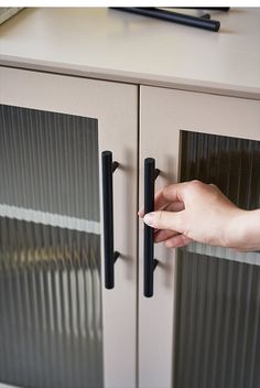 a hand is opening the door to a cabinet with glass doors and black handles on it