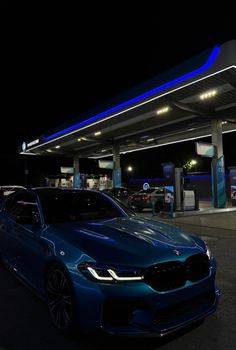 a blue car is parked in front of a gas station at night with its lights on