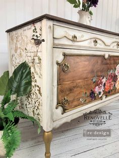 an old dresser with flowers painted on the side and gold trimmings, sits next to a potted plant