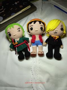 three small knitted dolls sitting next to each other on a white sheet with a book in the background