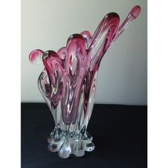 a pink glass vase sitting on top of a black table next to a white wall