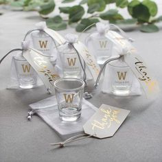 four personalized shot glasses and tags on a table with greenery in the background