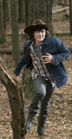 a young man is running through the woods wearing a cowboy hat and scarf on his head