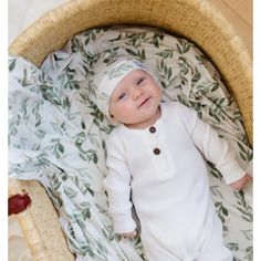 a baby laying in a wicker basket wearing a white outfit and headband with leaves on it