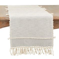 a white table runner with tassels on the edge and a wooden bench in the background