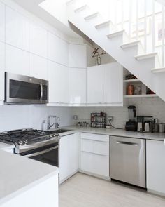 a white kitchen with stainless steel appliances and stairs leading up to the upper floor area