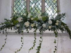 white flowers and greenery are arranged in a window sill with ivy on it