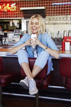 a woman sitting at a table with a cup in her hand and smiling while holding a drink