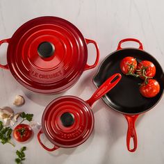 three red pots and pans with tomatoes on them