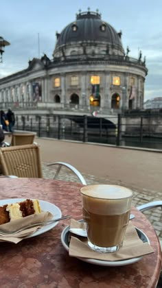 there is a cup of coffee and some food on the table in front of a building