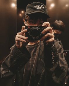 a man taking a selfie in front of a mirror with his camera and hat on