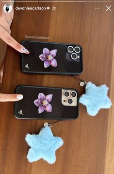 two iphone cases with flowers on them sitting on top of a wooden table next to someone's finger