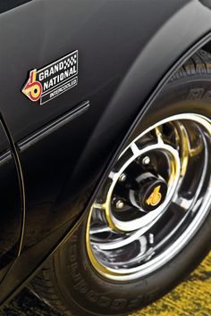 the front end of a black sports car with gold rims and logo on it