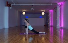 a woman is doing yoga on a mat in an empty room with purple lights behind her