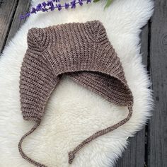 a knitted hat laying on top of a white fur rug next to purple flowers