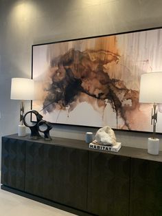 a large abstract painting hangs on the wall above a buffet table with two lamps in front of it