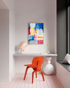 an orange chair sitting in front of a painting on a wall next to a window