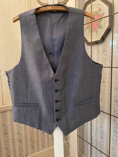 This classic vest looks grey from a distance, but up close it has black, white and medium blue fibres in the polyester blend fabric. It has the original buttons and two front pockets. The back and lining are made from silky bluish grey fabric. The measurements, taken with the vest lying flat, are: shoulder to shoulder, 13 inches; armpit to armpit, 22 inches; length, 25 inches in front and 21 inches in back; bottom edge, 22 inches. In very good condition. Affordable Gray Fitted Vest, Classic Tailored Gray Vest, Classic Fitted Gray Vest, Classic Gray Vest For Work, Gray Tailored Vest For Business, Fitted Gray Vest For Business, Gray Fitted Vest For Business, Fitted Gray Vest With Pockets, Classic Gray Formal Vest