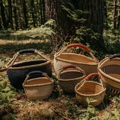 four woven baskets sitting next to a tree in the woods