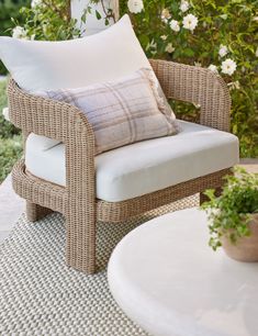 a wicker chair sitting on top of a white rug next to a table and flowers