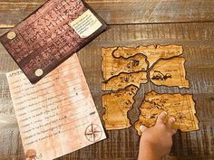 a person is pointing at an old map on a wooden table with other items around it