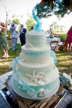 a wedding cake sitting on top of a table in front of other people and an umbrella