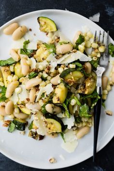 a white plate topped with beans and spinach next to a fork on top of a table