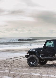 a black jeep parked on the beach next to the ocean with waves in the background