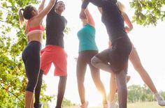 four people jumping up in the air with their arms around each other and trees behind them