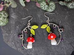 a pair of earrings with red and green mushrooms hanging from it's earwires