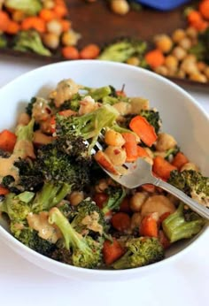 a white bowl filled with broccoli, chickpeas and carrots on top of a table