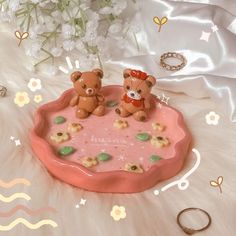 two teddy bears are sitting on a pink tray with flowers and rings around it,