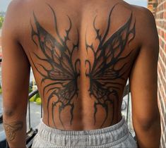 the back of a man with tattoos on his upper and lower body, standing in front of a brick wall