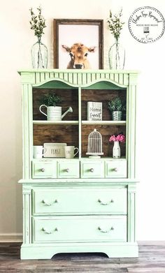 an old china cabinet painted green with white trim and flowers in vases on top