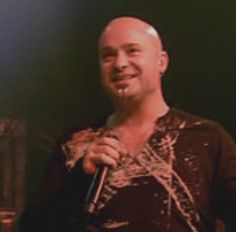 a bald man holding a microphone in his right hand and smiling at the camera while standing on stage