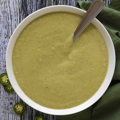 a white bowl filled with broccoli soup on top of a wooden table next to green peppers