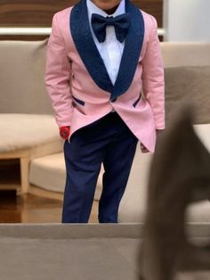 a young boy wearing a pink suit and bow tie standing in front of a couch