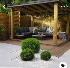 an outdoor living area with wooden pergoline and stone flooring, surrounded by shrubbery