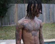 a man with dreadlocks standing in front of a swimming pool wearing no shirt