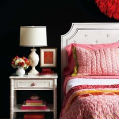 a white bed with pink and yellow comforter next to a table with flowers on it