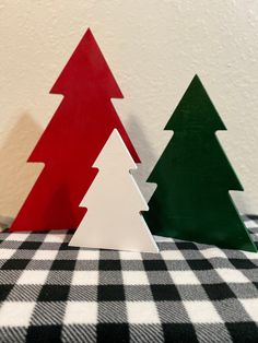 three wooden christmas trees sitting on top of a black and white checkered table cloth