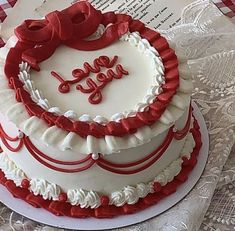 a white and red cake sitting on top of a table next to an open book