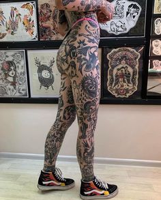 a woman with tattoos standing in front of a wall full of tattoo designs on her body