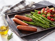 sausages, asparagus and potatoes on a baking sheet with olive oil in the background