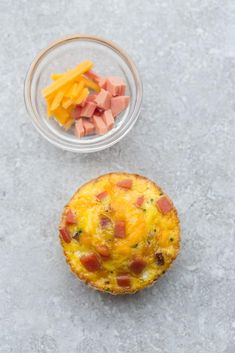 a muffin with ham and cheese on it next to a bowl of diced fruit