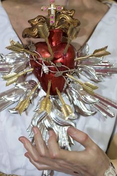 a woman holding a red heart shaped vase with gold leaves on it's sides