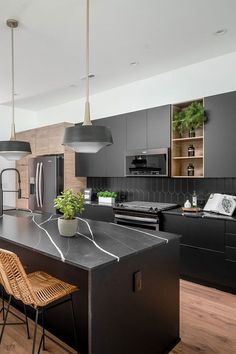 a kitchen with black cabinets and wooden flooring, two pendant lights hanging over the island