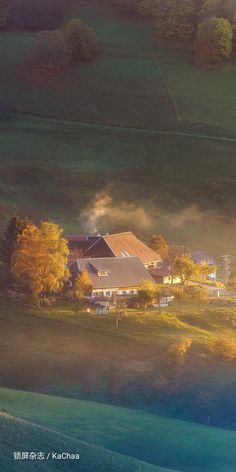 an aerial view of a farm house surrounded by trees in the foggy morning light