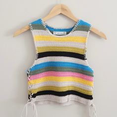 a multicolored striped knitted top hanging on a wooden hanger next to a white wall