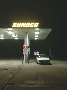 a white car is parked in front of a sunoco gas station sign at night